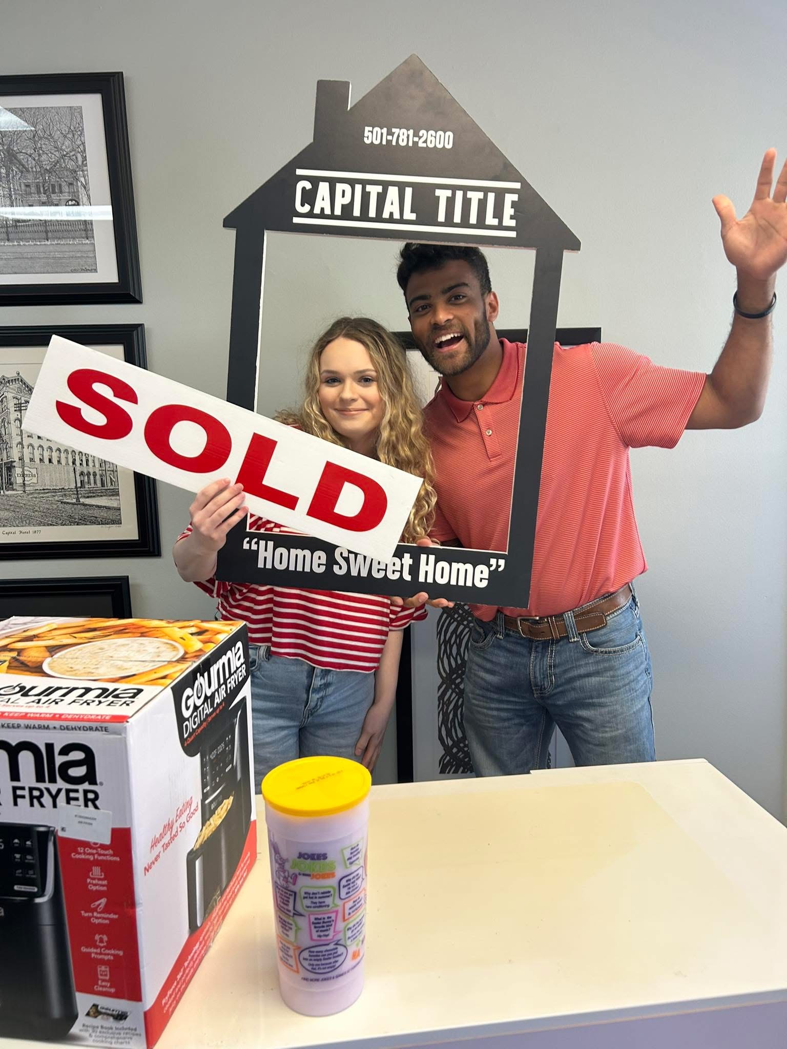 Madison Burke and client holding a sold sign with a Capital Title frame